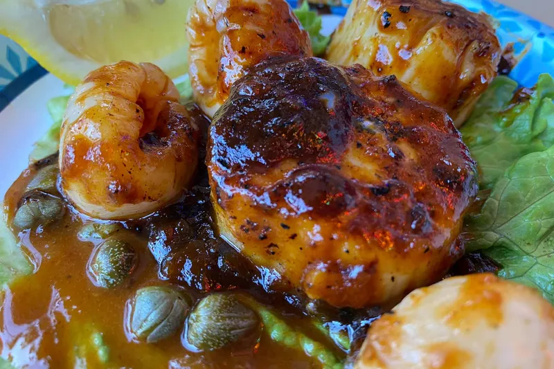 Close-up of grilled sea scallops and shrimp glazed in sauce over lettuce with capers on a plate at The Turf Club