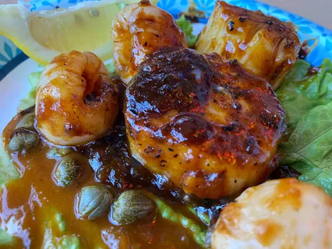 Close-up of grilled sea scallops and shrimp glazed in sauce over lettuce with capers on a plate at The Turf Club