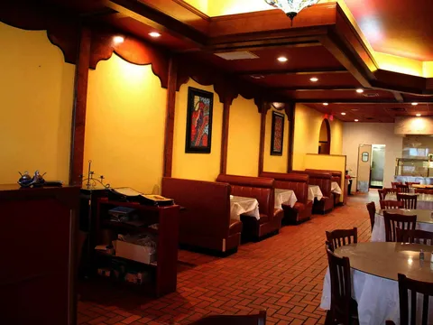 Interior dining room at Curry Bliss in Richardson with red leather booths, yellow walls, Indian artwork, and cloth-topped tables