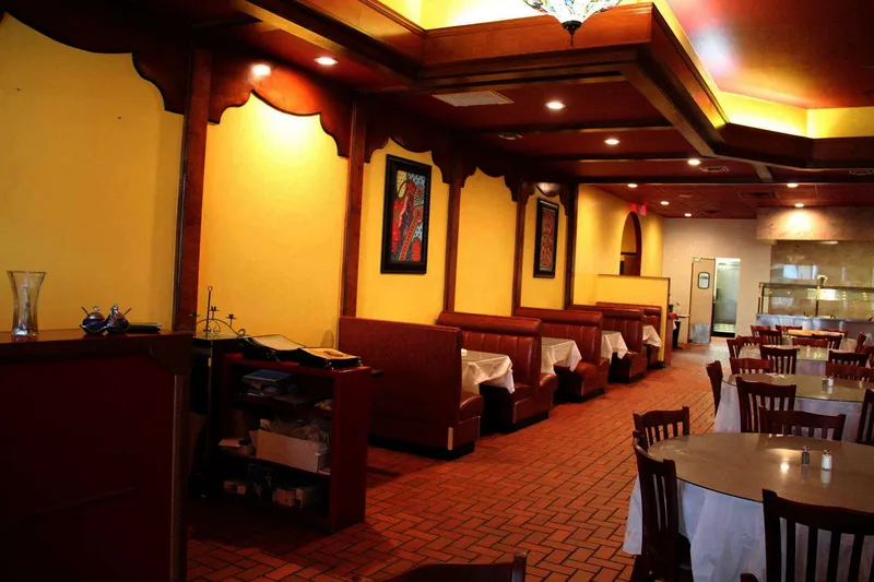 Interior dining room at Curry Bliss in Richardson with red leather booths, yellow walls, Indian artwork, and cloth-topped tables