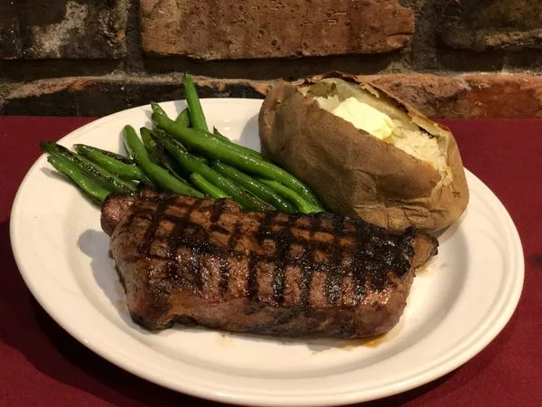Charbroiled steak with green beans and a baked potato on a white plate at Mancini's Char House