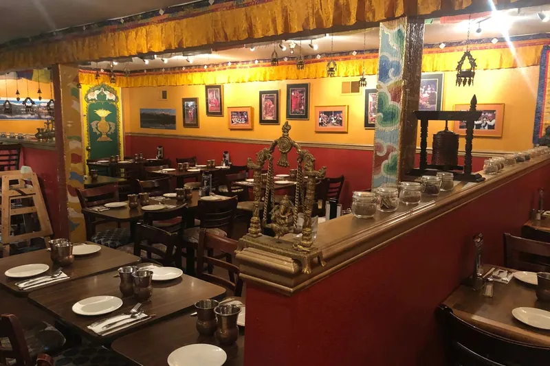 Dining room at Annapurna Cafe, with red walls, framed photographs, a brass shrine and set tables