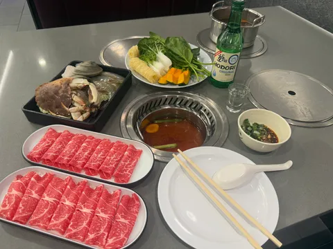 Hot pot spread at Hotpot One in Quincy with platters of sliced marbled beef, seafood and vegetables around a broth-filled pot on a grill table