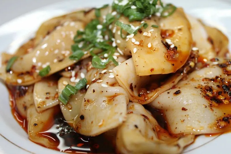 Plate of pork Zhong-style dumplings in chili oil topped with scallions and sesame seeds at Gu's Dumplings