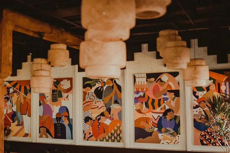 Andina's dining room in Portland with colorful painted murals of Andean scenes beneath woven pendant lamps
