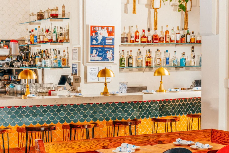 Bar at Fish Cheeks in NoHo, Manhattan, with green and yellow fish-scale tiles, brass dome lamps and a backbar of liquor bottles