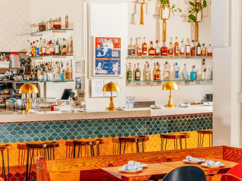 Bar at Fish Cheeks in NoHo, Manhattan, with green and yellow fish-scale tiles, brass dome lamps and a backbar of liquor bottles