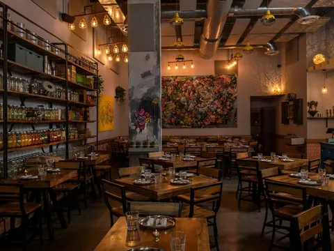 Warmly lit Ghee Indian Kitchen dining room with wooden tables and a colorful spice display