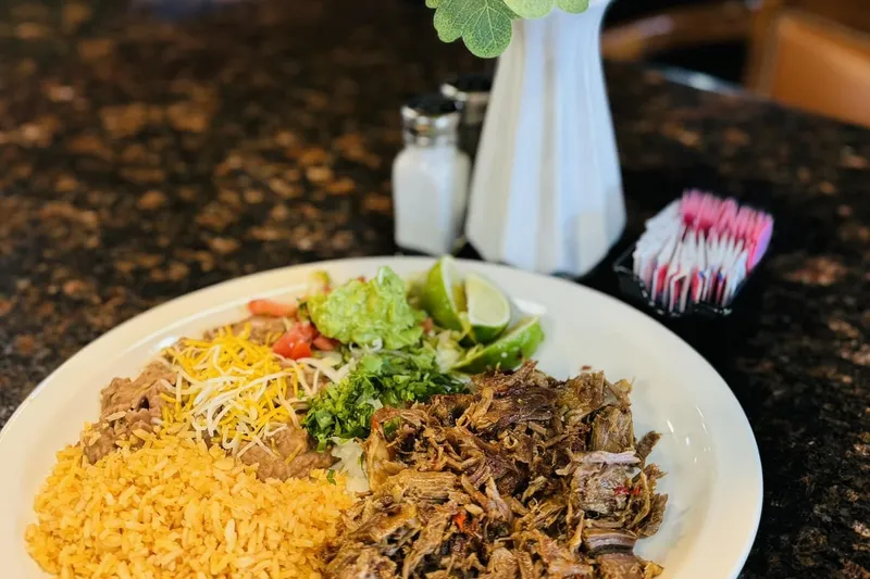 Carnitas plate with Mexican rice, refried beans topped with cheese, guacamole, pico de gallo and lime at Tacos El Charrito in Denver