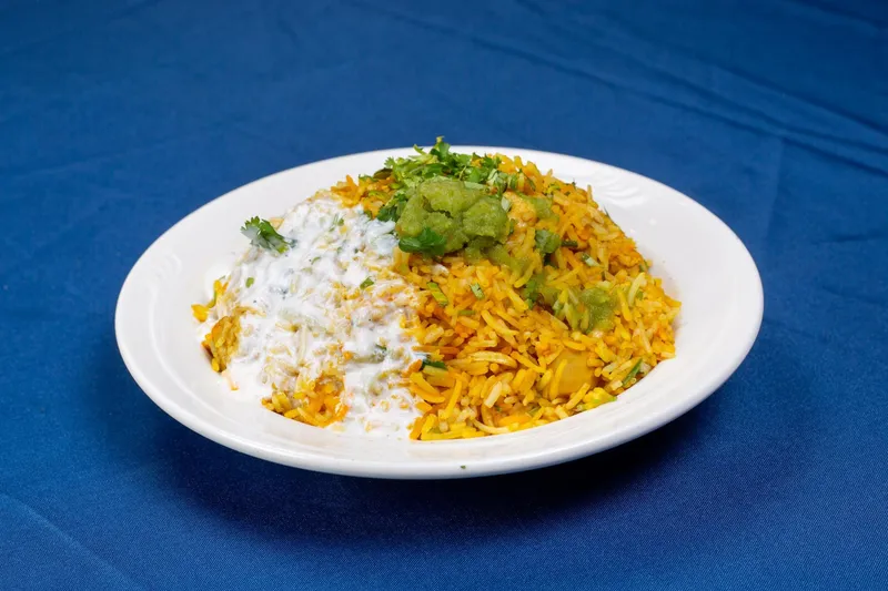 Plate of chicken biryani topped with cilantro and green chutney with a side of raita, on a blue tablecloth, at India Star in Des Moines
