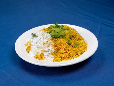 Plate of chicken biryani topped with cilantro and green chutney with a side of raita, on a blue tablecloth, at India Star in Des Moines