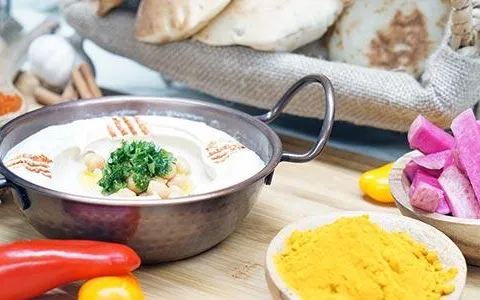 Al Ameer's hummus topped with chickpeas and parsley in a copper dish, served with pita bread, pickled turnips, and spices