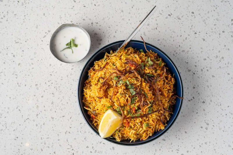 Bowl of biryani with lemon and raita, seen from above, at Tabla