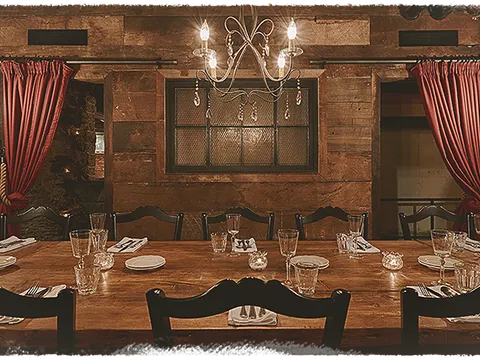 Rustic private dining room at Sotto with a long reclaimed-wood table set with glassware under a chandelier and red drapes