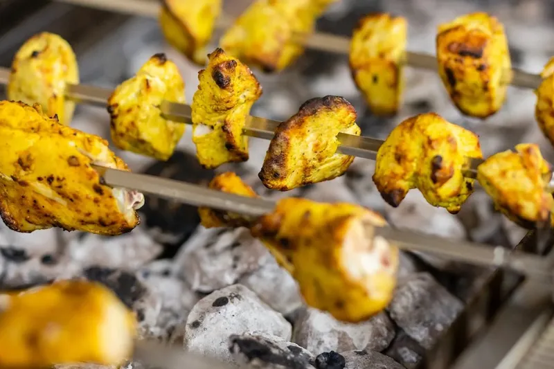 Skewers of marigold-yellow tandoori chicken tikka cooking over glowing charcoal at Star of India in Salt Lake City