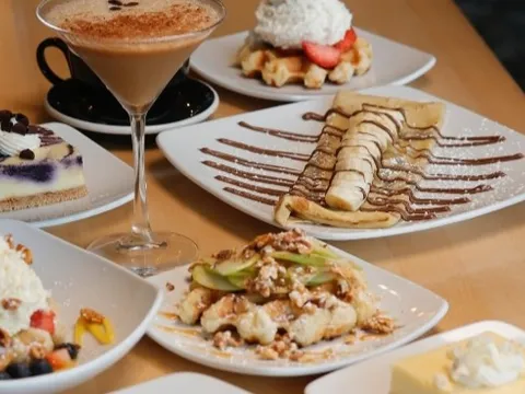 Spread of Taste of Belgium desserts including a Liège waffle with strawberries, a chocolate-drizzled crêpe, cheesecake and an espresso martini on a wood table