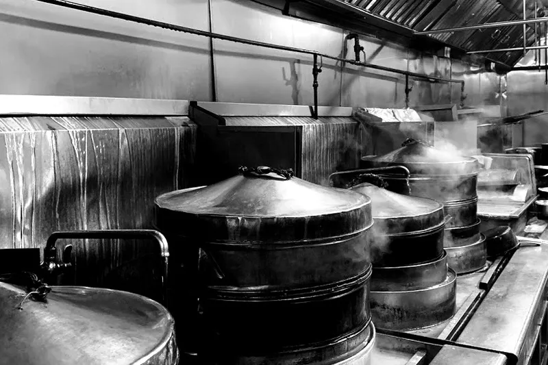Black-and-white photo of the Jasmine Seafood kitchen line, with rows of large stacked bamboo-and-metal dim sum steamers venting steam
