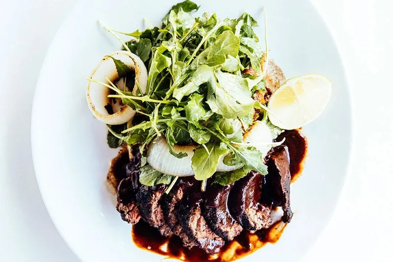 Plated grilled sliced steak with mole-style sauce, charred onion and arugula at El Barrio in Birmingham, Alabama