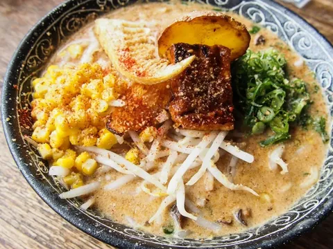 A bowl of Facing East paitan ramen topped with charred char siu, seasoned corn, bean sprouts, scallions and a bamboo shoot in a creamy broth