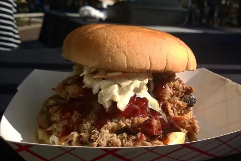 Hickory smoked pulled pork sandwich topped with coleslaw and BBQ sauce in a paper boat at Eli's BBQ