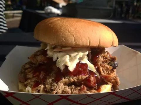 Hickory smoked pulled pork sandwich topped with coleslaw and BBQ sauce in a paper boat at Eli's BBQ