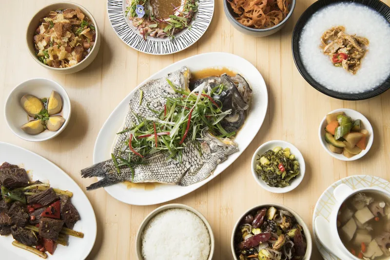Overhead spread of Pinch Chinese dishes including whole steamed fish with scallions, cumin beef, congee, braised eggs and rice