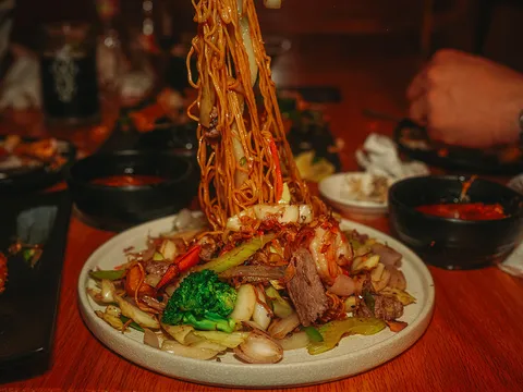 A plate of Viet-Cajun stir-fry with garlic noodles lifted high above shrimp, beef, broccoli and cabbage at Crawfish & Noodles in Houston