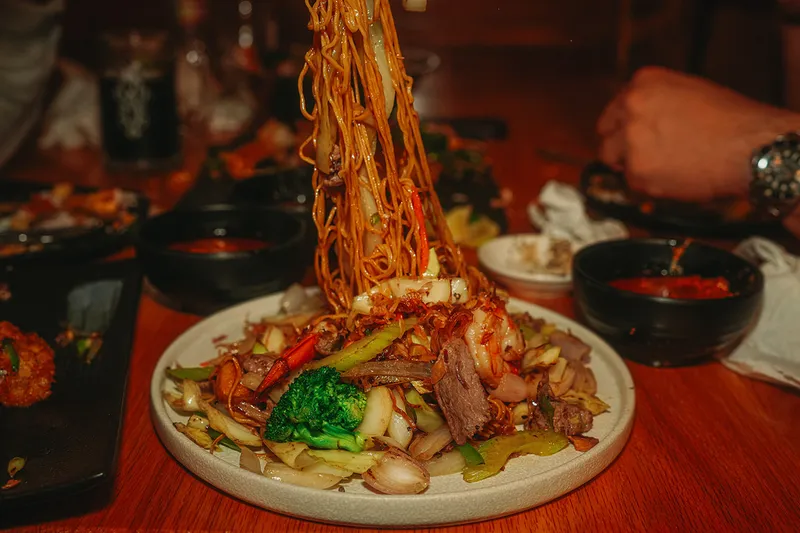 A plate of Viet-Cajun stir-fry with garlic noodles lifted high above shrimp, beef, broccoli and cabbage at Crawfish & Noodles in Houston