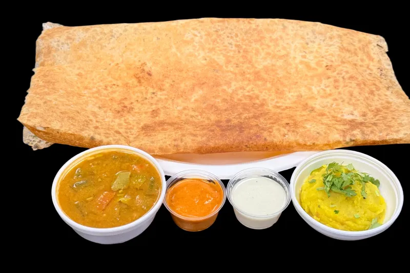 A crispy golden masala dosa served with sambar, tomato and coconut chutneys and potato masala in takeout cups at Saffron Cafe in Norcross.
