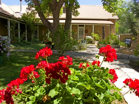 Flagstone courtyard with red geraniums leading to the historic adobe restaurant and hacienda at Rancho de Chimayó in Chimayó, New Mexico