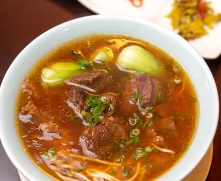 Bowl of Facing East Taiwanese beef noodle soup with braised beef, baby bok choy and scallions, served with side condiments