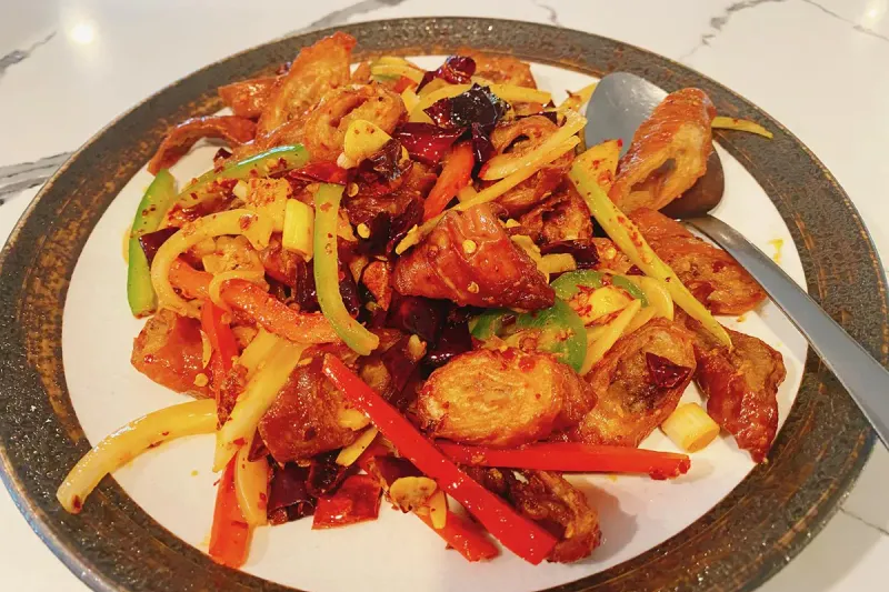 Sichuan-style wok-fried dish with dried chilies, sliced peppers and ginger on a plate at Cooking Girl