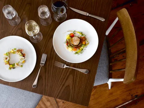 Two plated seasonal dishes with wine glasses on a walnut table at Persimmon in Providence