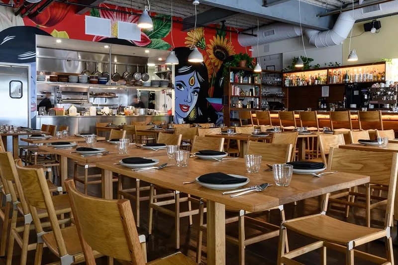 Besharam dining room with wooden tables, open kitchen and colorful wall art