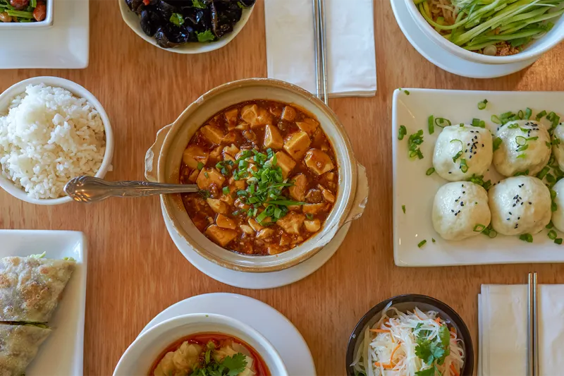 Overhead spread of Pine & Crane Taiwanese dishes including mapo tofu, panfried pork buns, dan dan noodles, beef roll and rice