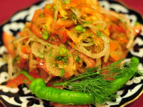 Achichuk-style tomato and onion salad garnished with dill and a green chili on a traditional patterned plate at Cafe Kashkar