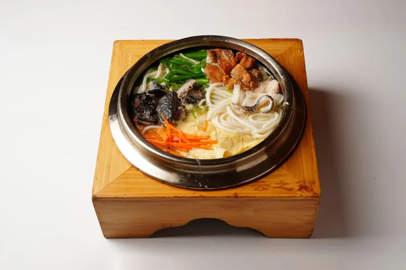 Yunnan crossing-the-bridge rice noodles served in a metal bowl on a branded wooden stand at South of the Clouds (云之南), Greenwich Village
