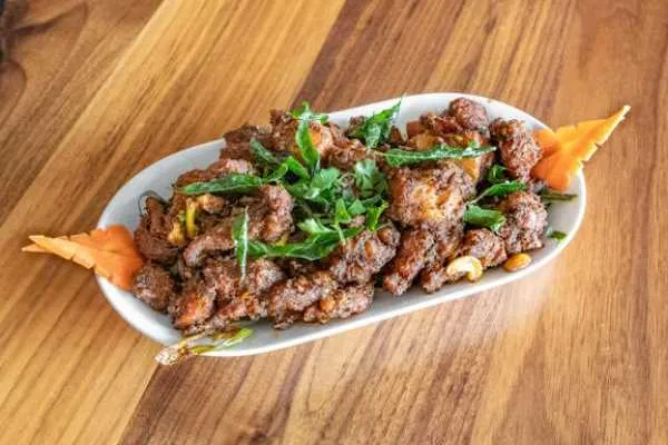Bawarchi Andhra-style curry-leaf chicken fry plated with fresh herbs
