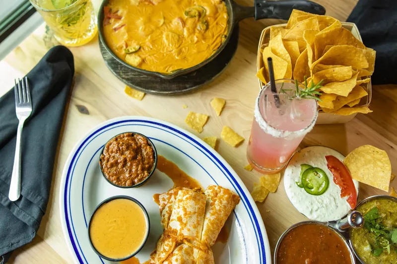 Spread of melting-pot cheese dip, tamales with chili and queso, tortilla chips, salsas and cocktails at Heights Taco & Tamale Co. in Little Rock, Arkansas