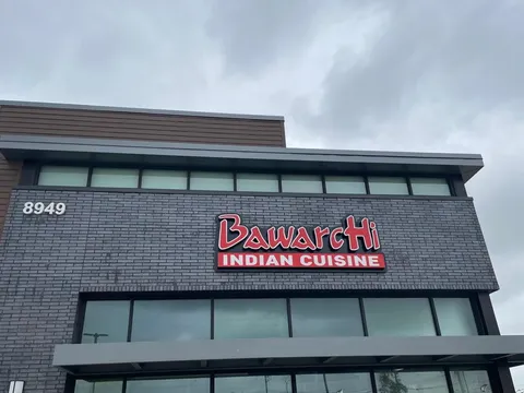 Exterior of Bawarchi Indian Cuisine (East Frisco) — a grey-brick two-story building with a red 'BawarcHi Indian Cuisine' sign and the address number 8949 — in Frisco, Texas