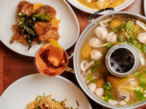 Spread of Lotus of Siam dishes, including a curry, a tom yum hot pot, and crispy seafood, on a wooden table
