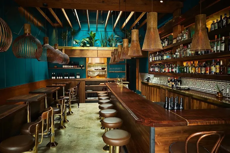 Bar at Rupee Bar, with teal panelling, brass pendant lights and a row of stools
