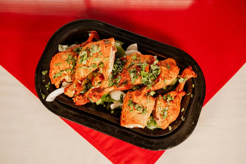 Tandoori chicken pieces garnished with cilantro served on a black platter at Amul India Restaurant