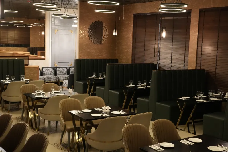 The dining room at Bombay Bistro in Redmond, with set tables, tall green upholstered booths, gold accents and ring pendant lights